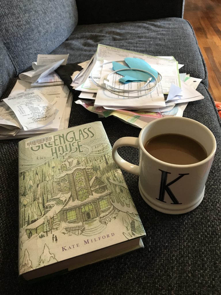 A coffee mug and a book in the foreground, with miscellaneous papers and receipts in stacks in the background