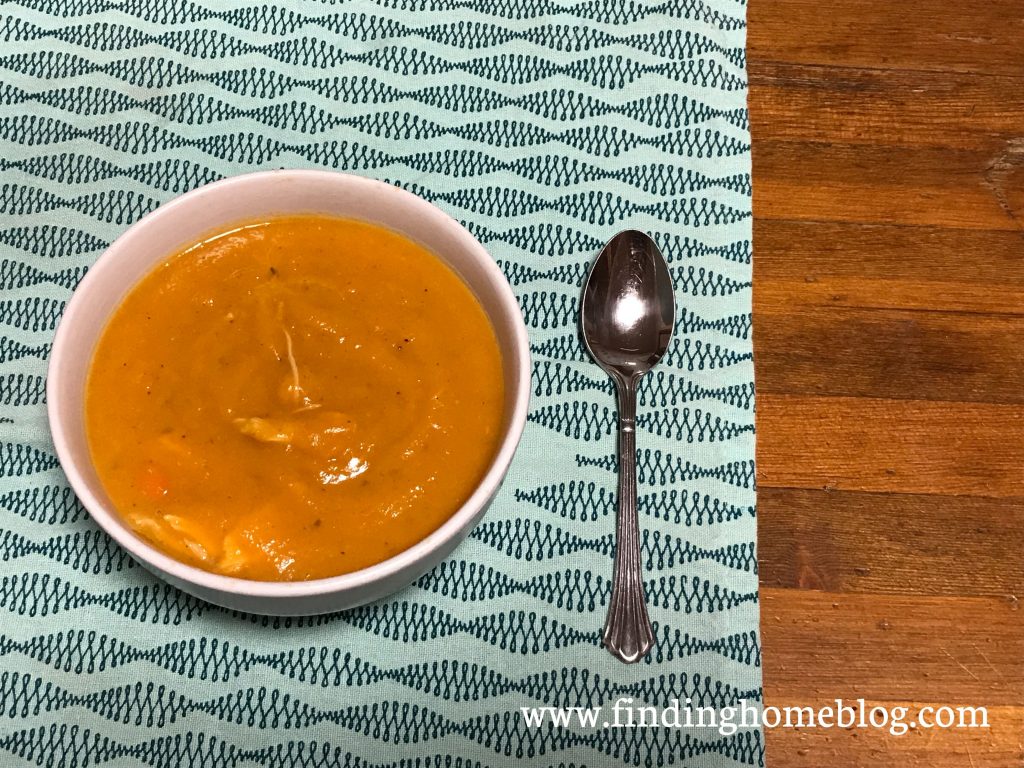 A bowl of vibrant orange soup on a blue patterned cloth with a spoon next to it