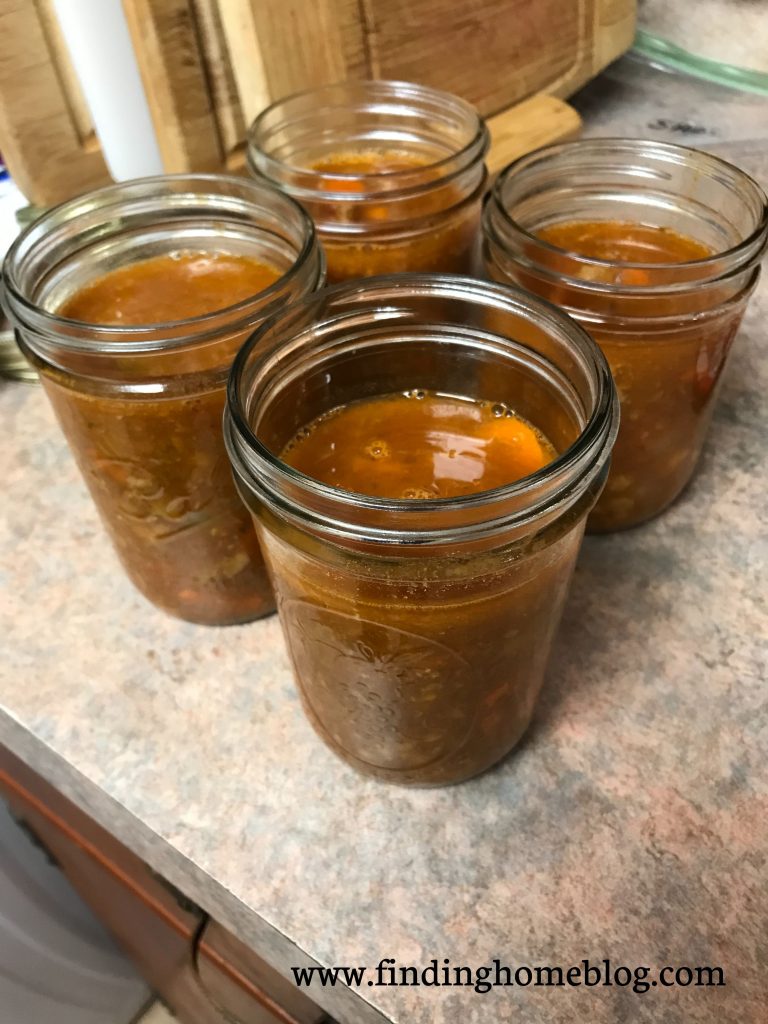 Four jars of a turkey tomato soup sitting on a counter next to some cutting boards.