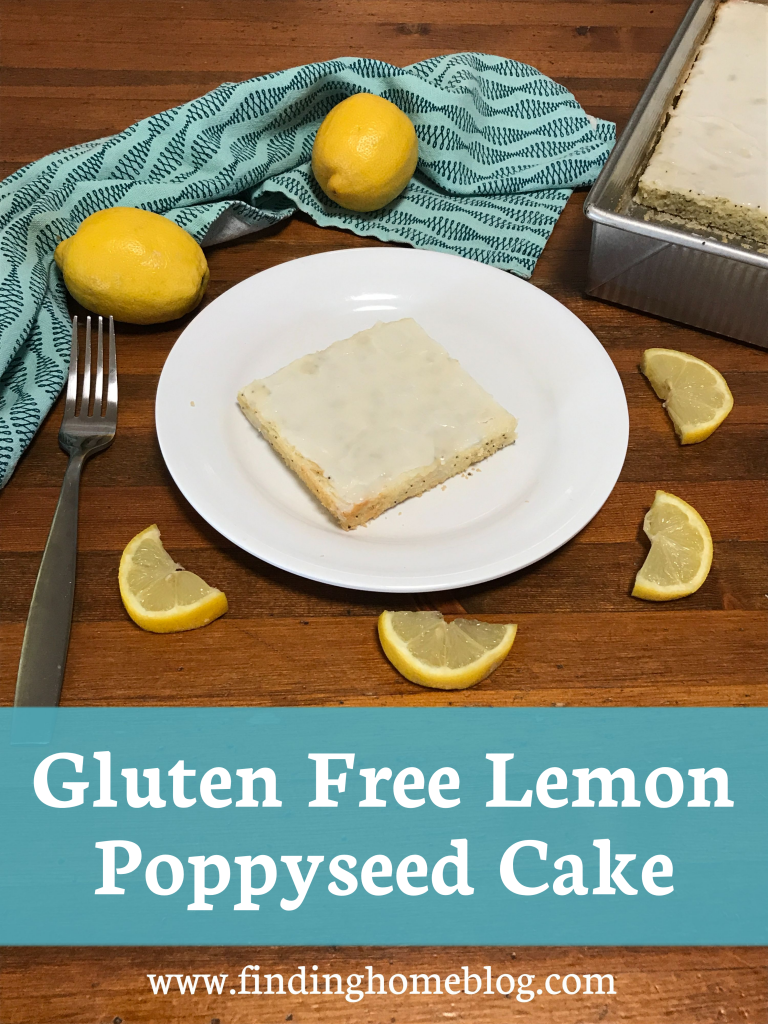 A piece of lemon cake on a plate, surrounded by lemon slices, whole lemons, a cloth napkin, and the pan of cake. A banner across the bottom reads "Gluten Free Lemon Poppyseed Cake".