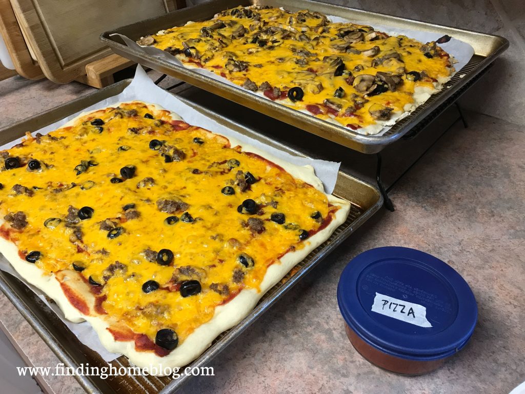 Two freshly baked pizzas on rectangular pans with a small container of sauce next to them.