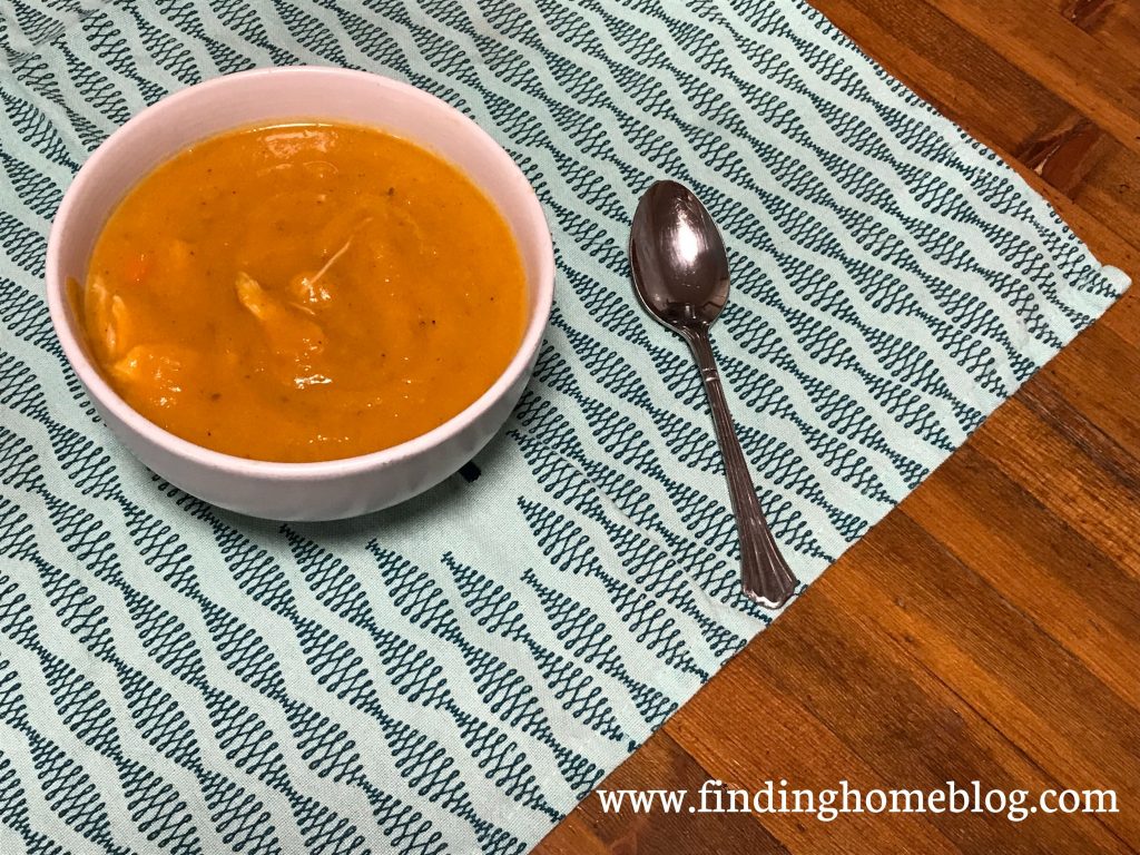 A bowl of vibrant orange soup on a blue patterned cloth with a spoon next to it