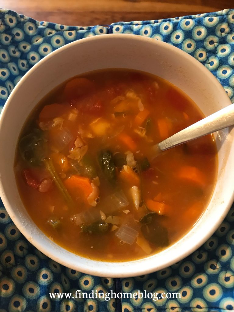 Close up on a bowl of tomato vegetable soup with a spoon sticking out of the side of it.