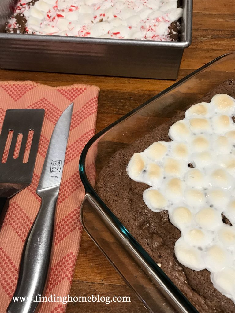 A pan of marshmallow topped brownies next to a cloth napkin with a knife and spatula on it.