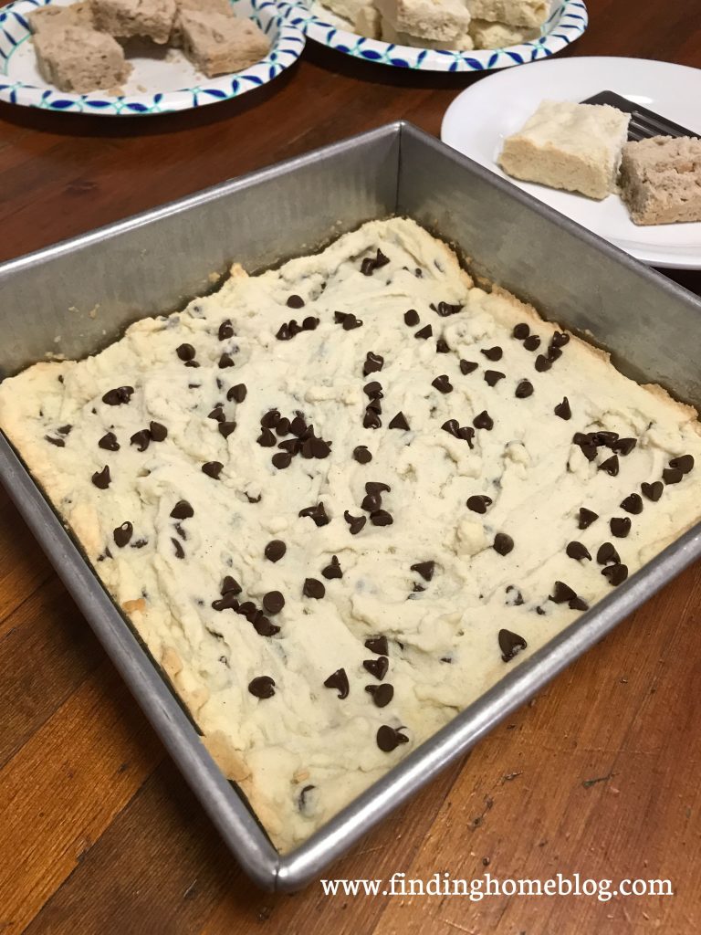 Close up on a metal square pan with chocolate chip shortbread bars inside. Several bars on plates in the background.