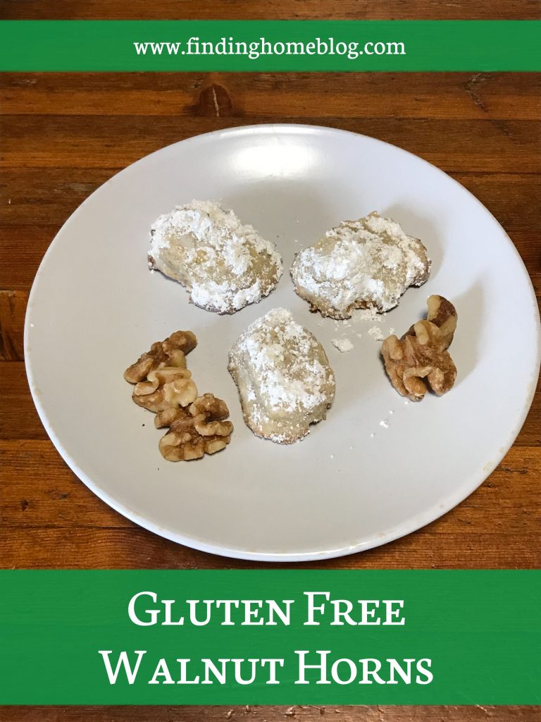 Three cookies, coated with powdered sugar, on a plate, along with some walnuts