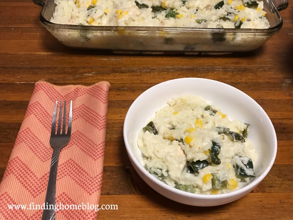 A bowl with a rice casserole in the foreground; a cloth napkin and fork off to the left. A 13x9 pan with more casserole in the background.