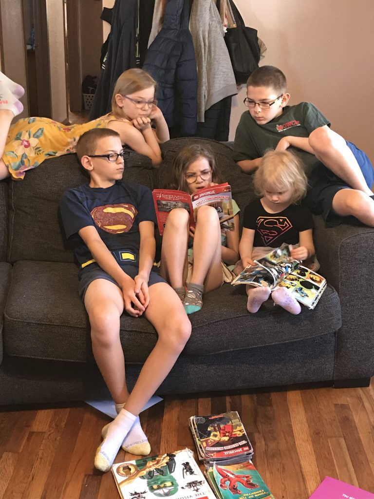 Five kids reading books together on a couch.