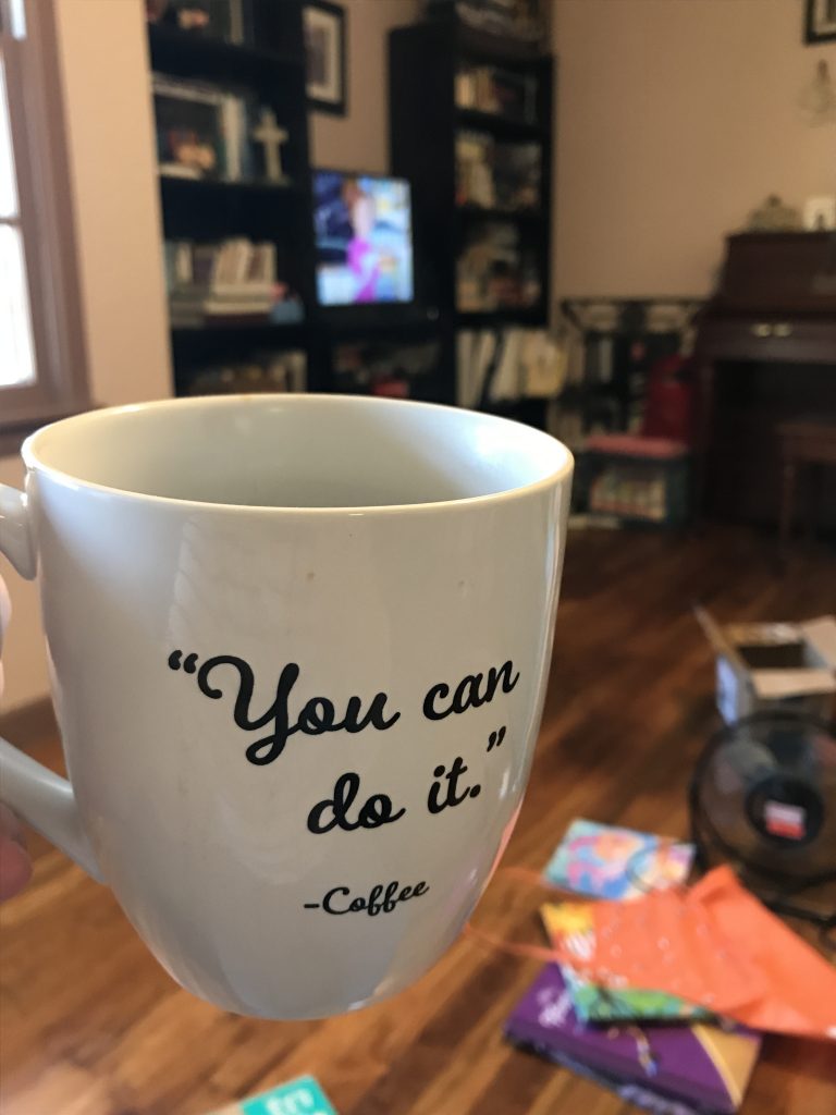 A close up of a coffee mug that says "You can do it. - Coffee", with the television on in the background, playing The Magic School Bus.