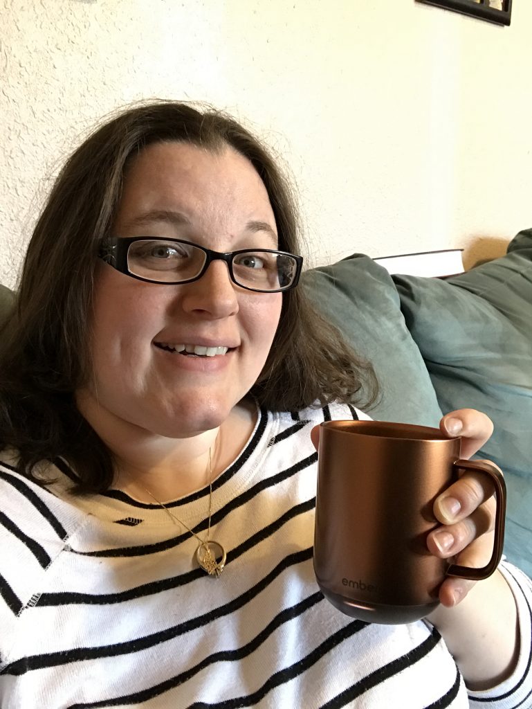 A woman smiling and holding an Ember coffee mug.