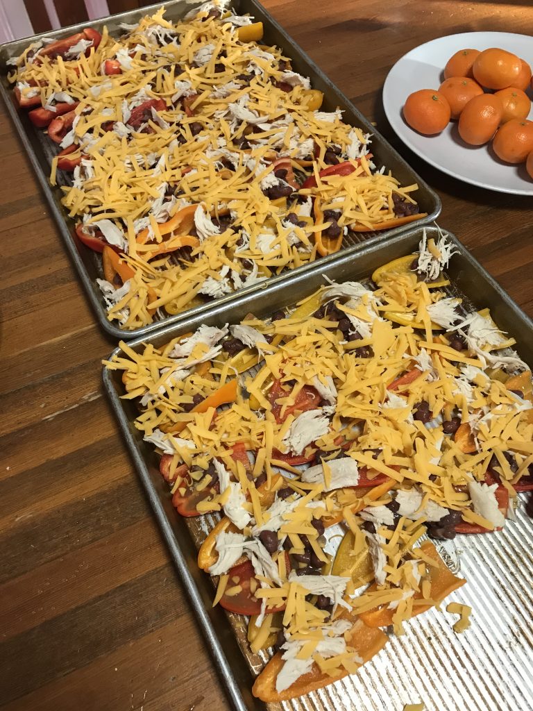 Two sheet pans of nacho toppings on halved mini peppers, before being baked.