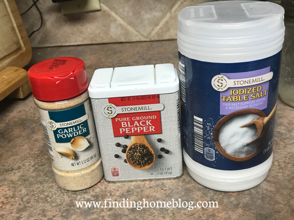 Containers of garlic powder, black pepper, and salt on a kitchen counter