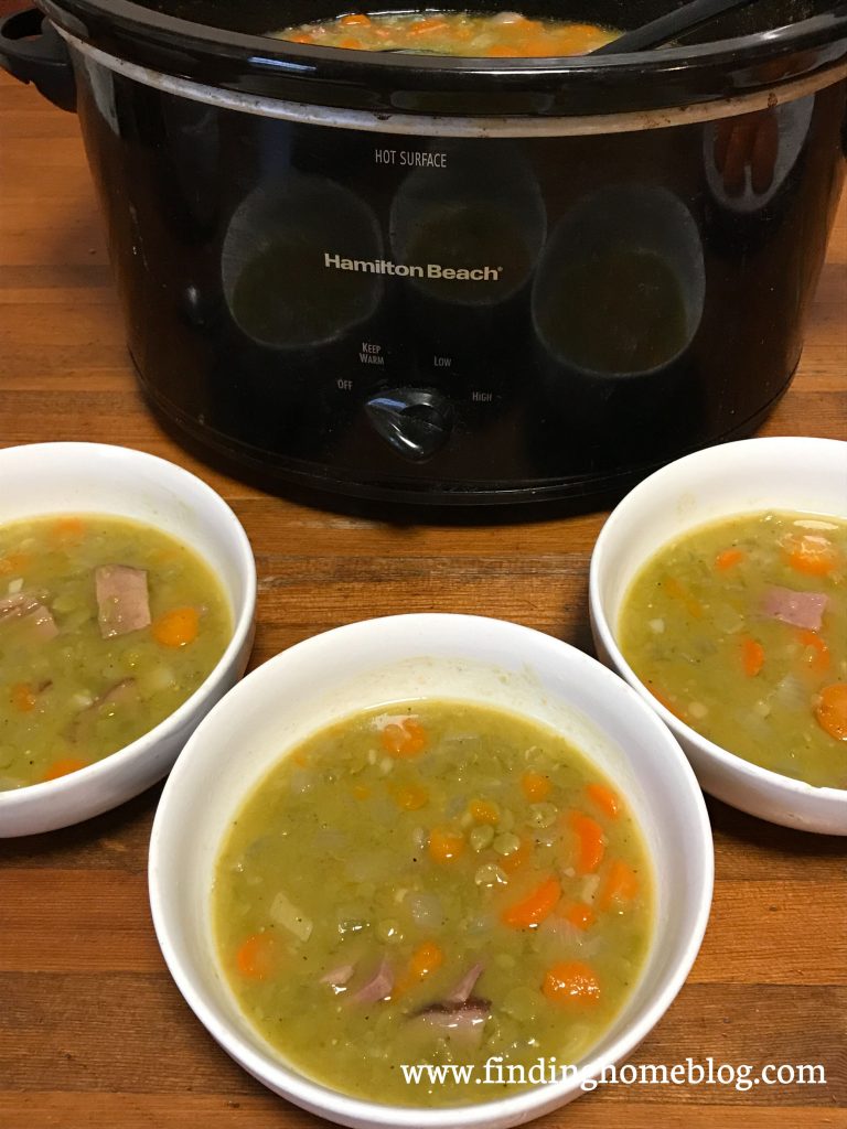 A crockpot full of split pea soup in the background with a ladle sticking out of it. Three bowls of soup dished out in the foreground