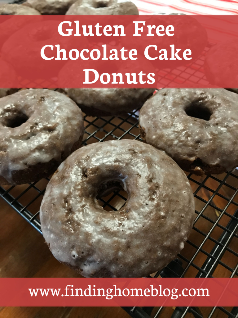 A close up of glazed chocolate cake donuts on a cooling rack. A banner reads "Gluten Free Chocolate Cake Donuts".